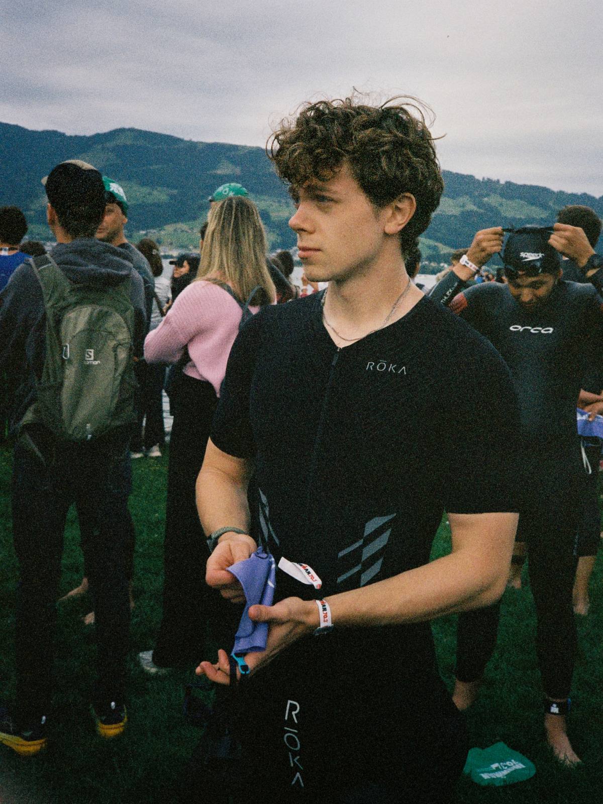 Aidan in a ROKA race suit at a lakeside race start, holding his swim cap